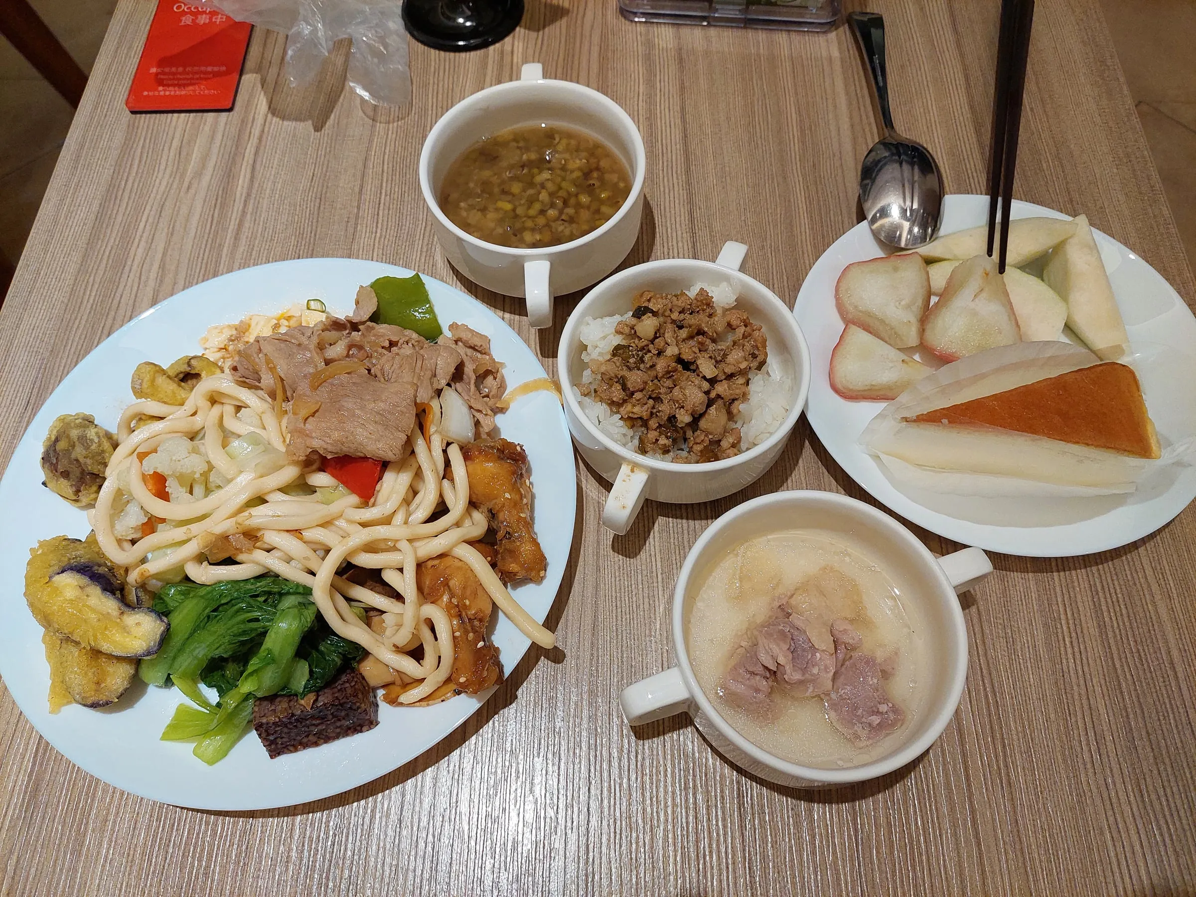 Fried noodles, vegetables, rice with minced pork, soup, fruit and cake on a table