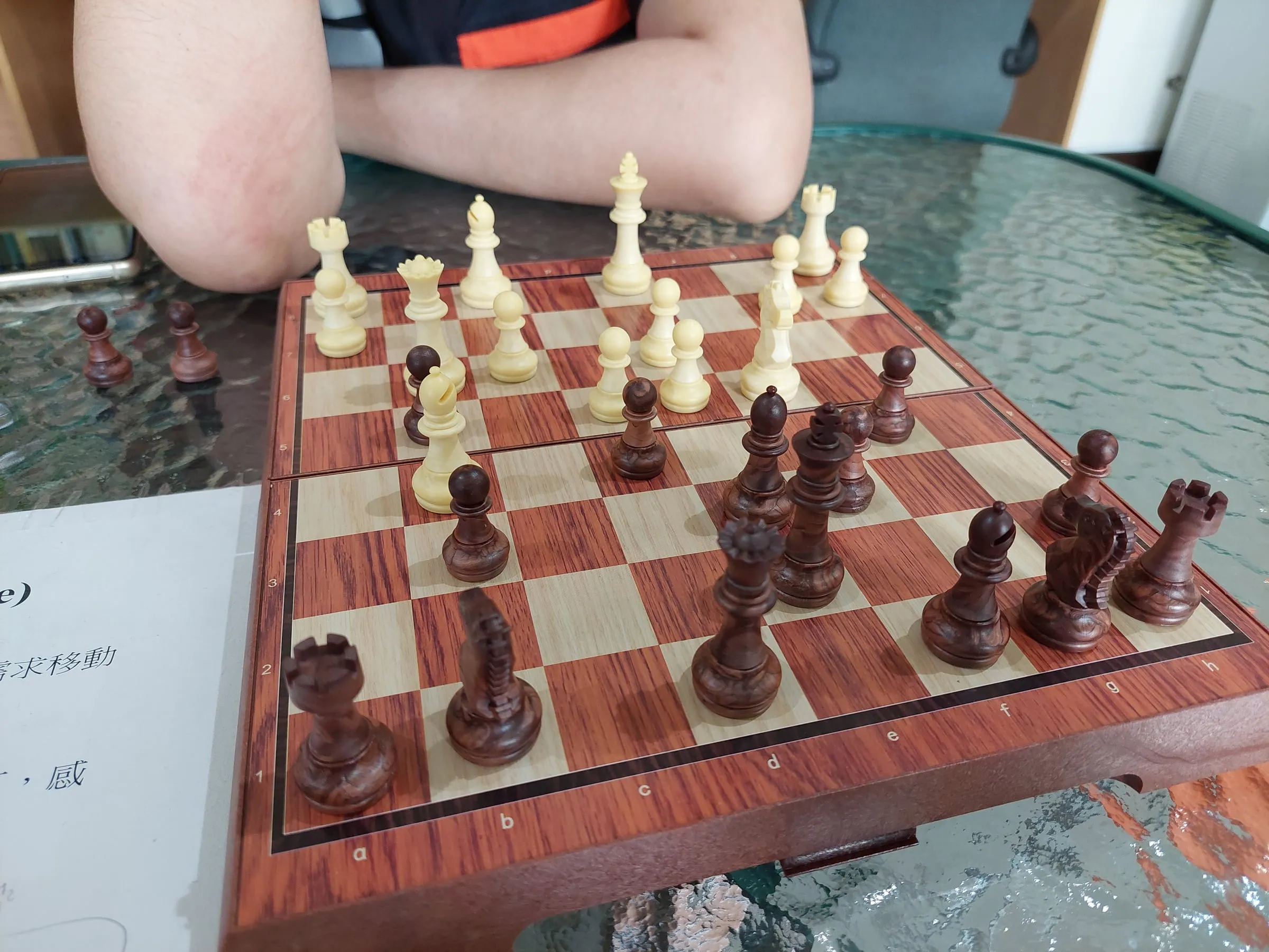 A chessboard on a glass table, with the opponent's arms folded, waiting for the next move