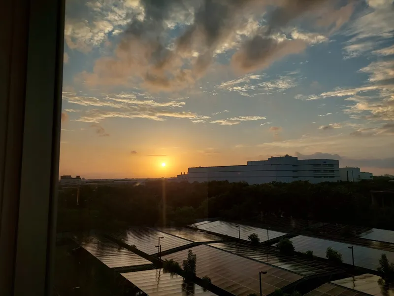 View from a window as the sun sets behind distant buildings