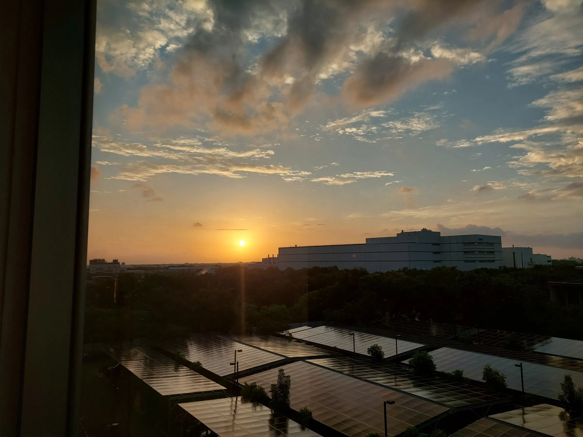 View from a window as the sun sets behind distant buildings