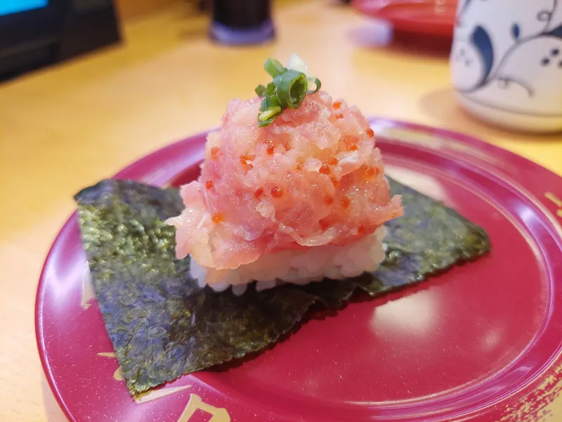 A gunkan sushi piled with minced tuna and fish roe on a red plate