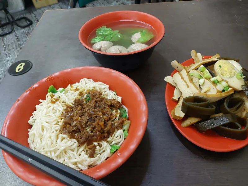 A bowl of dry noodles with minced pork, a bowl of meatball soup and a plate of braised snacks