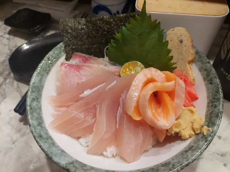 A bowl topped with salmon and white fish sashimi, garnished with a shiso leaf and kumquat