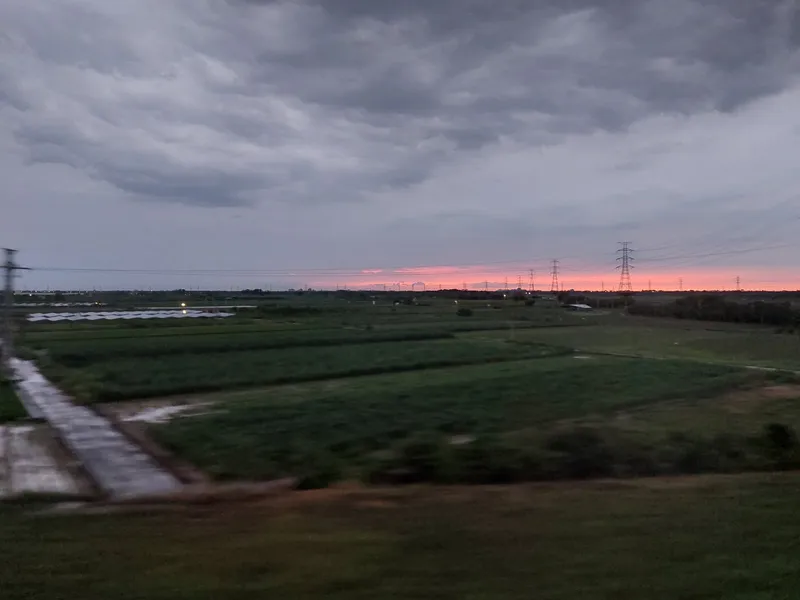 An overcast dusk with a band of pink on the horizon, above wide fields and power pylons