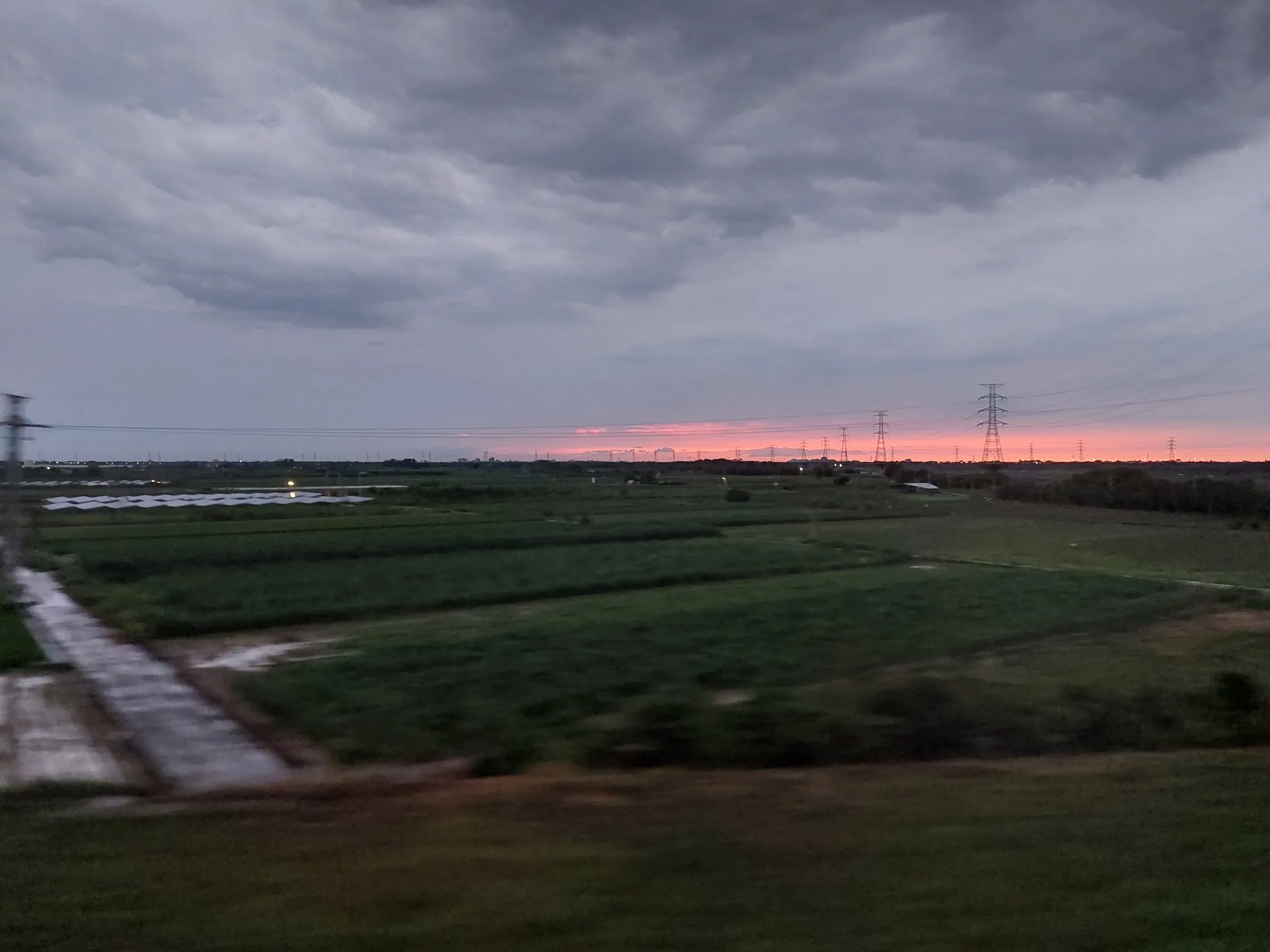 An overcast dusk with a band of pink on the horizon, above wide fields and power pylons