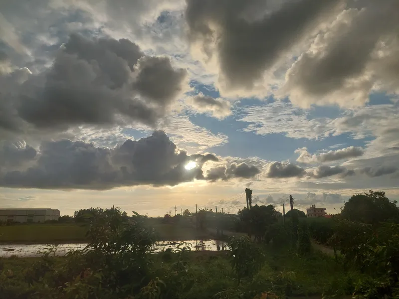 Thick clouds covering the sun, with light breaking through the gaps above trees and fields