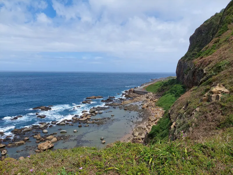 Looking down from a hillside at a rocky coastline with waves breaking along it