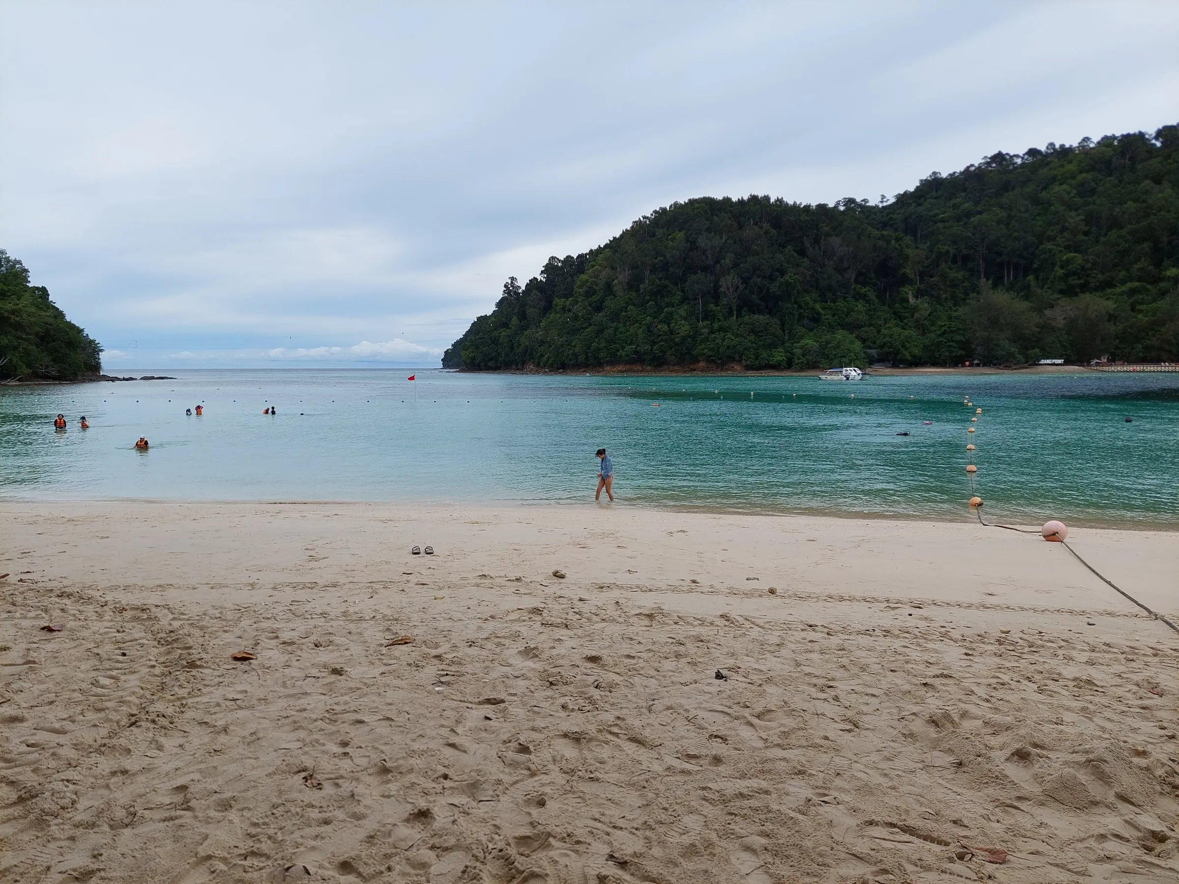 A white sand beach and clear shallow water, facing a forested island