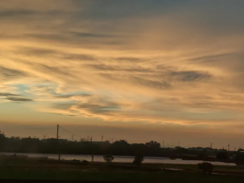 An evening sky full of golden clouds above a silhouetted riverbank and trees