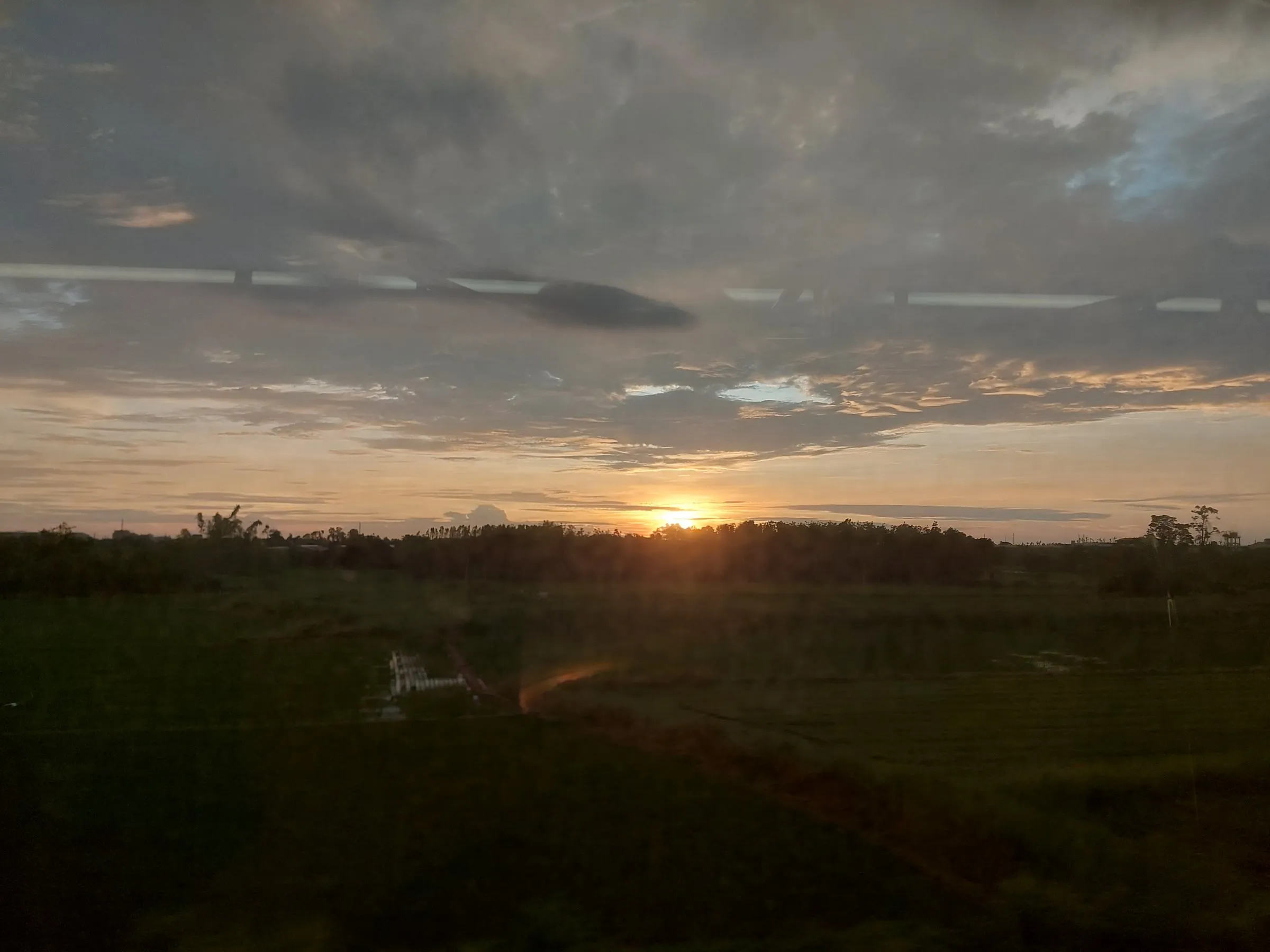 The sun sinking near the horizon under a layer of grey clouds