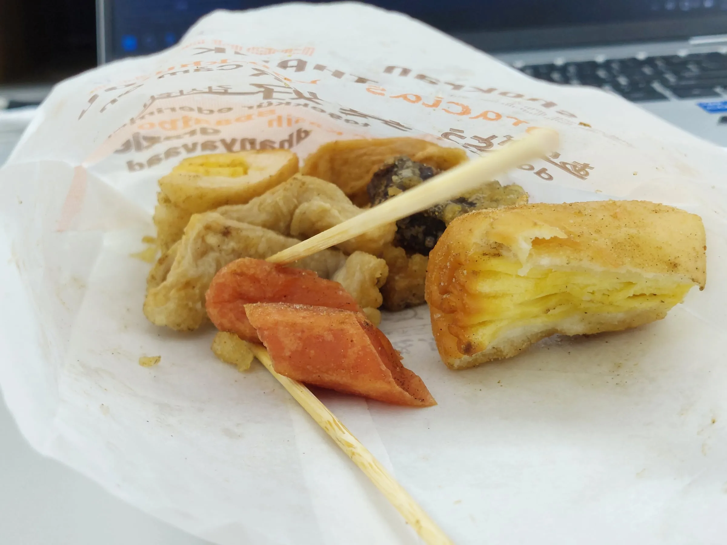 A paper bag of assorted fried snacks, including fried tofu and fish cakes