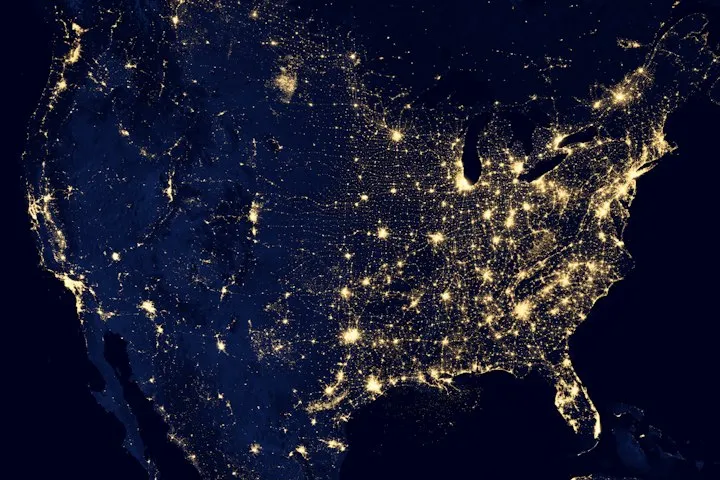 Satellite view of the contiguous United States at night, showing glowing city lights against a dark Earth