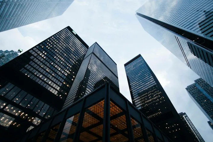 Low-angle view looking straight up at dark glass skyscrapers against a pale overcast sky