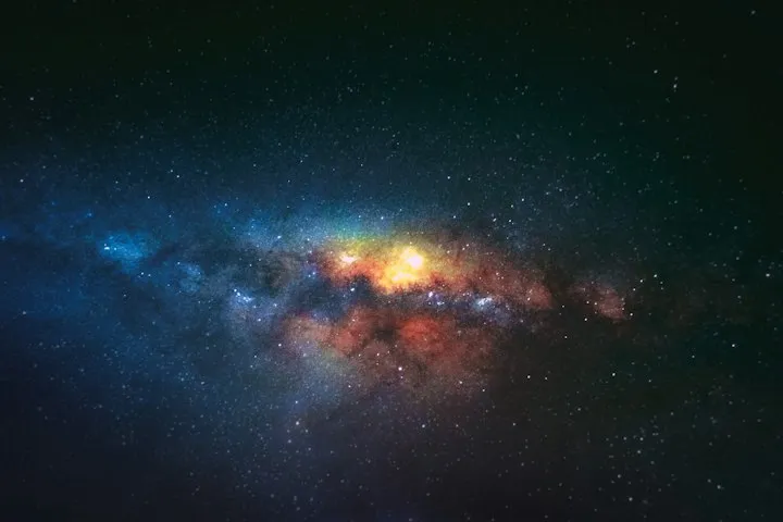 Long-exposure photograph of the Milky Way galactic core with yellow, orange, and blue star clouds