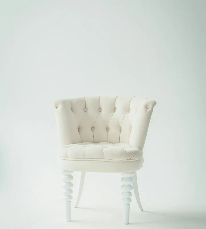 Cream button-tufted armchair with decorative white turned legs against a plain light gray studio background