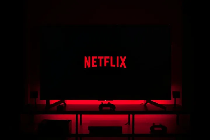 Television in a dark room displaying the red Netflix logo with red ambient backlighting